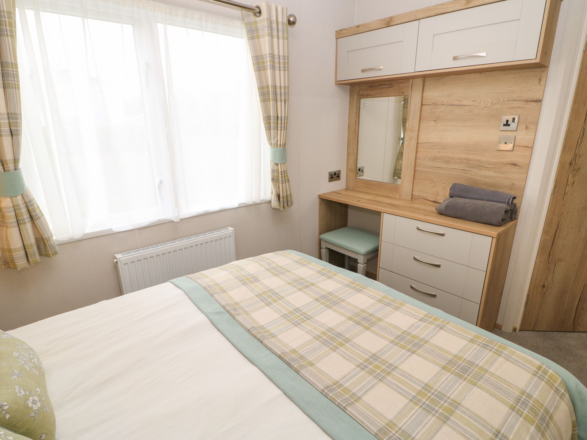 A bedroom with a bed, a desk, a mirror, and a radiator.