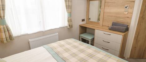 A bedroom with a bed, a desk, a mirror, and a radiator.
