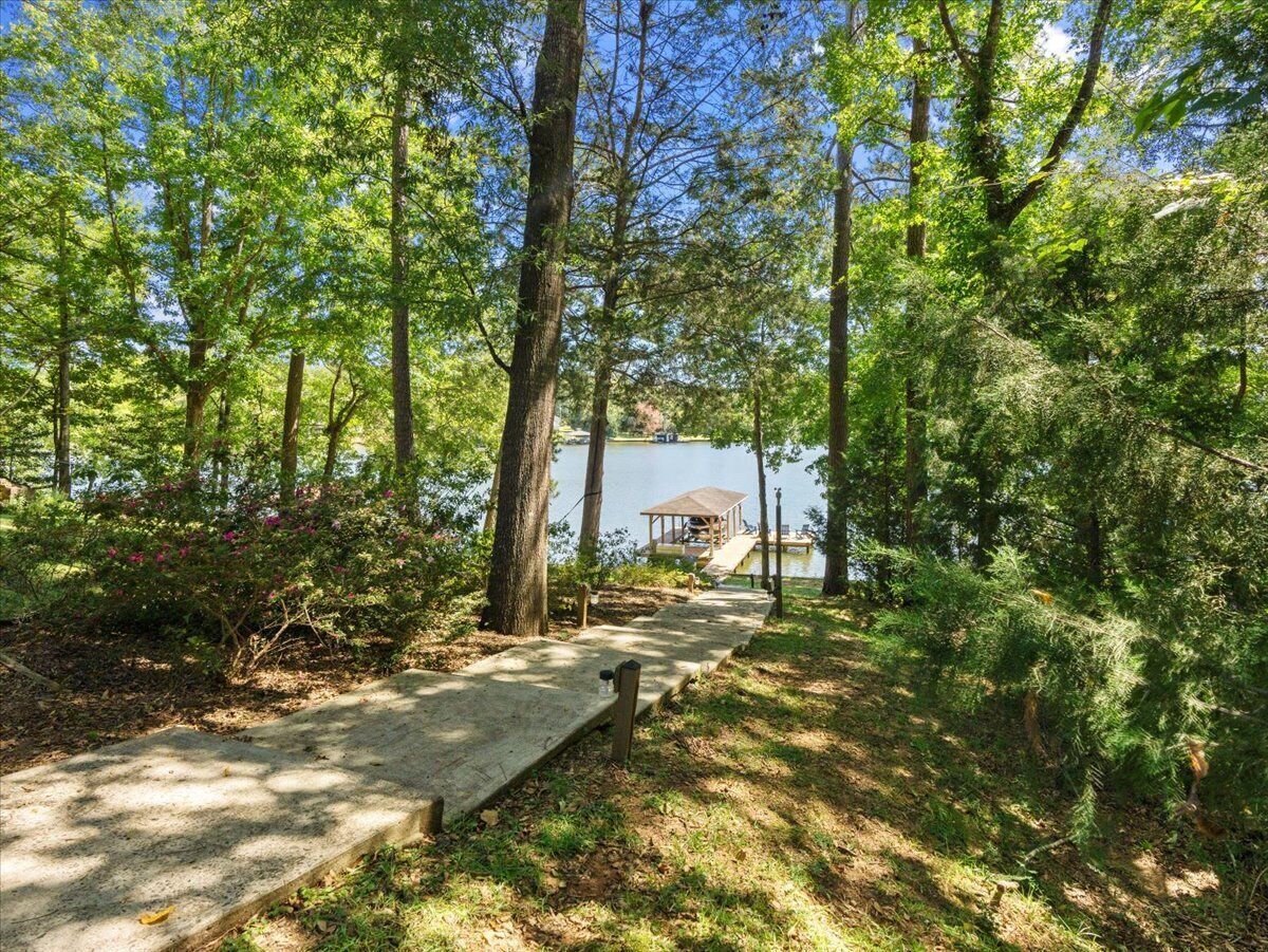 A concrete pathway leading to a dock over a body of water, surrounded by dense green foliage.
