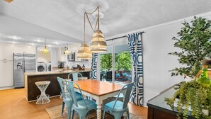 Una cocina moderna con una isla central, luces colgantes y una zona de comedor con sillas azules.