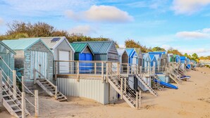 A row of beach huts with wooden stairs leading up to each, situated on a sandy beach. - Trem Ynys (Pwllheli)