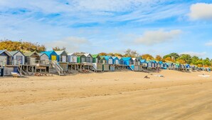 A row of beach huts with wooden structures and blue roofs, situated on a sandy beach. - Trem Ynys (Pwllheli)