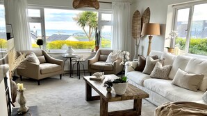 A spacious living room with a view of the sea, featuring a sofa set, a coffee table, and a lamp. - Trem Ynys (Pwllheli)