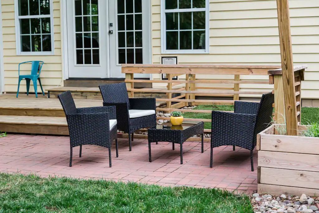 An outdoor patio with wicker furniture, a wooden bench, and a small table with a potted plant.