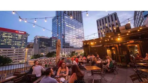 An outdoor dining area with tables and chairs, surrounded by city buildings and string lights. - The City Cottage, pet friendly, walk to shops, food & NCSU (Raleigh)