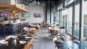 A modern restaurant with a bar area, multiple tables, and chairs, and large windows offering a view. - The City Cottage, pet friendly, walk to shops, food & NCSU (Raleigh)