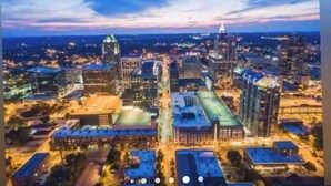 An aerial view of a cityscape at dusk with prominent buildings, roads, and a large open area. - The City Cottage, pet friendly, walk to shops, food & NCSU (Raleigh)