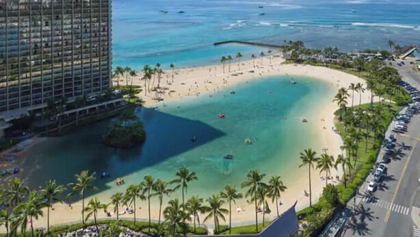 Um hotel na praia com um edifício grande, uma praia de areia e águas azul-claras.