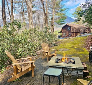 A wooden deck with Adirondack chairs and a stone fire pit.