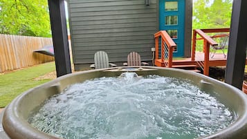Een hottub onder een overdekte veranda met een houten terras, een blauwe deur en tuinmeubilair.