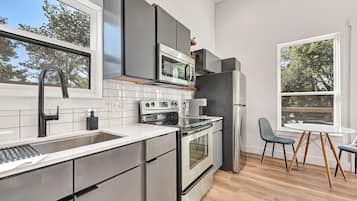 Een moderne keuken met roestvrijstalen apparatuur, een groot raam en een eethoek met een ronde tafel en stoelen.