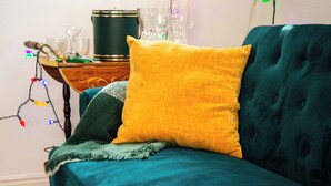 Un sofá color turquesa con un cojín amarillo y una manta verde.