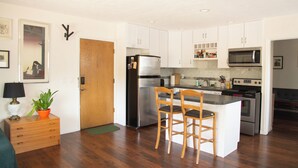 Una cocina funcional con alacenas blancas, un refrigerador de acero inoxidable, un microondas y un horno. Hay dos sillas de madera en la isla de la cocina.