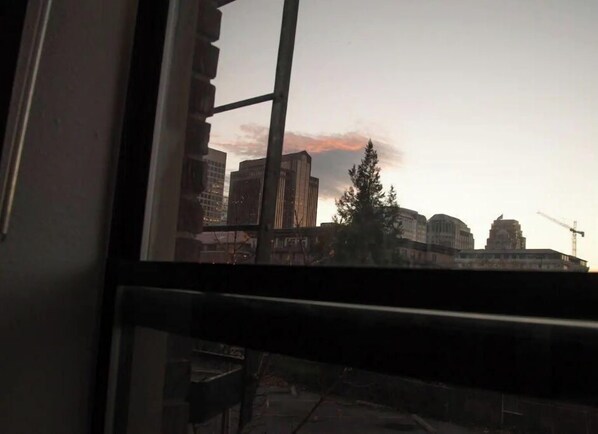 En vy genom ett fönster som visar en stadsbild i skymningen, med byggnader och en byggkran synliga.