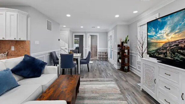 Una sala de estar moderna con un sofá blanco, cojines azules, una mesa de centro de madera y un televisor de pantalla plana grande.