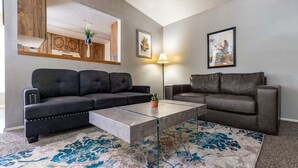 Un salon avec deux canapés en cuir foncé, une table basse en verre et un tapis à motifs.