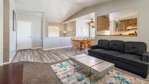 Un salon spacieux avec un canapé foncé, un coin repas avec des chaises en bois et une cuisine avec des meubles en bois.
