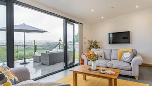 Una sala de estar moderna con un sofá gris, una mesa de centro de madera y un ventanal con vistas a un balcón.