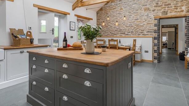 Una cocina con isla central, vigas de madera, pared de piedra y tragaluz.