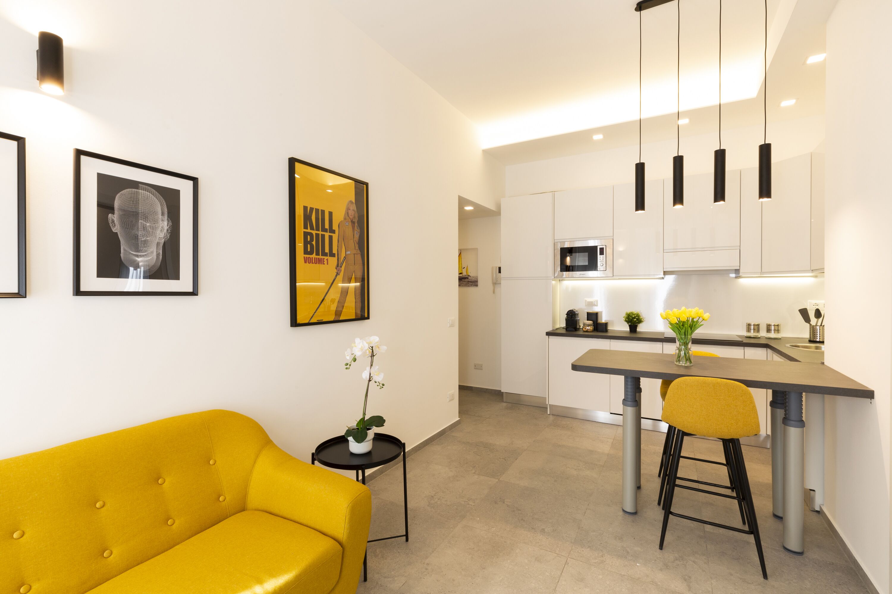 A modern kitchen with a central island, a yellow sofa, and a small side table with a plant.