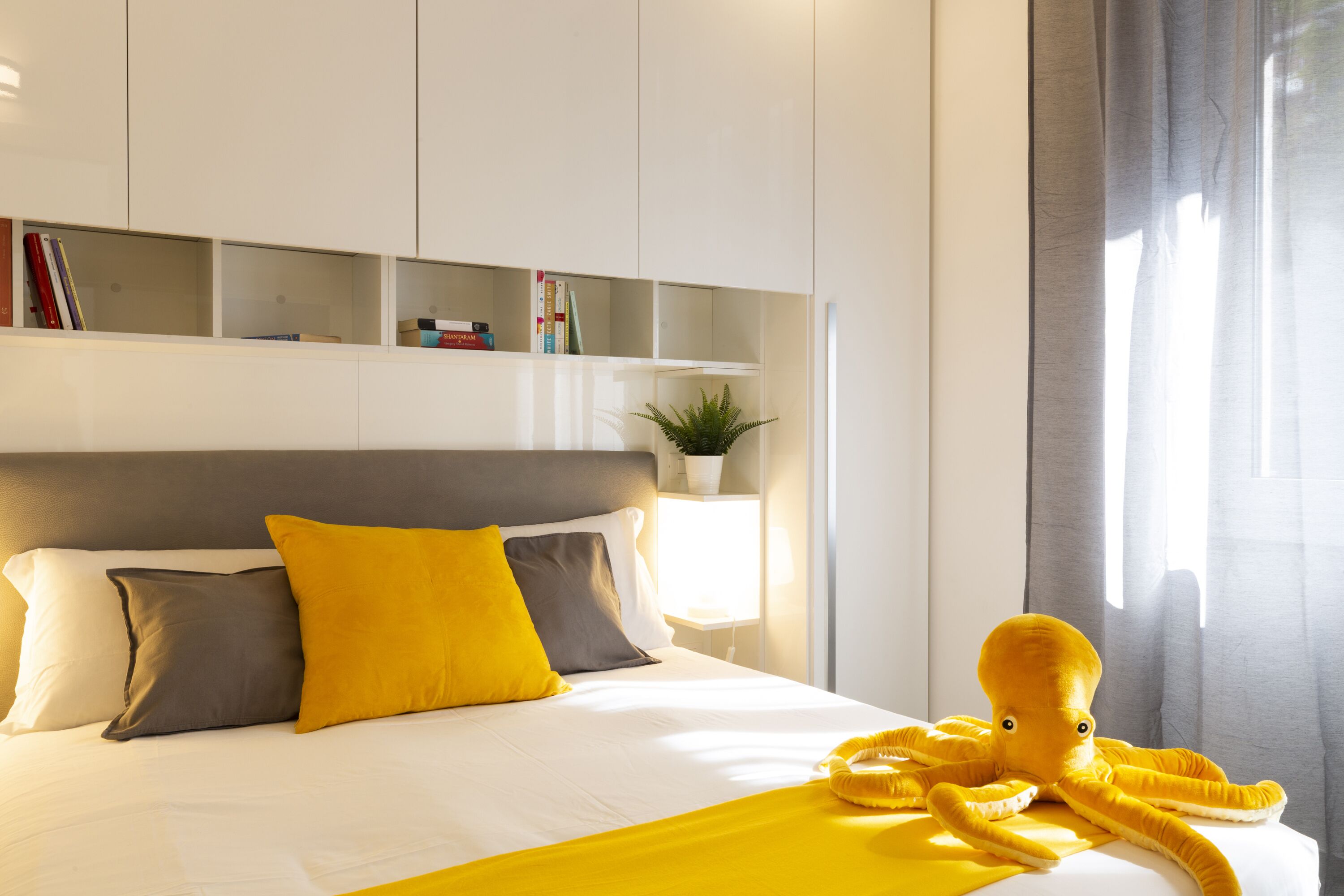 Un lit bien fait, avec une tête de lit, une table de chevet avec une lampe et une étagère avec des livres et une plante.