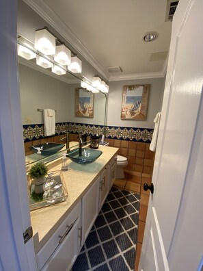 Un baño con un lavabo de cristal, un perchero, un inodoro y un salpicadero decorativo de azulejos.