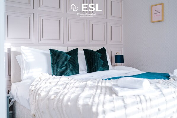 A neatly made bed with white and teal bedding, a blue throw blanket, and a wall with a framed quote.