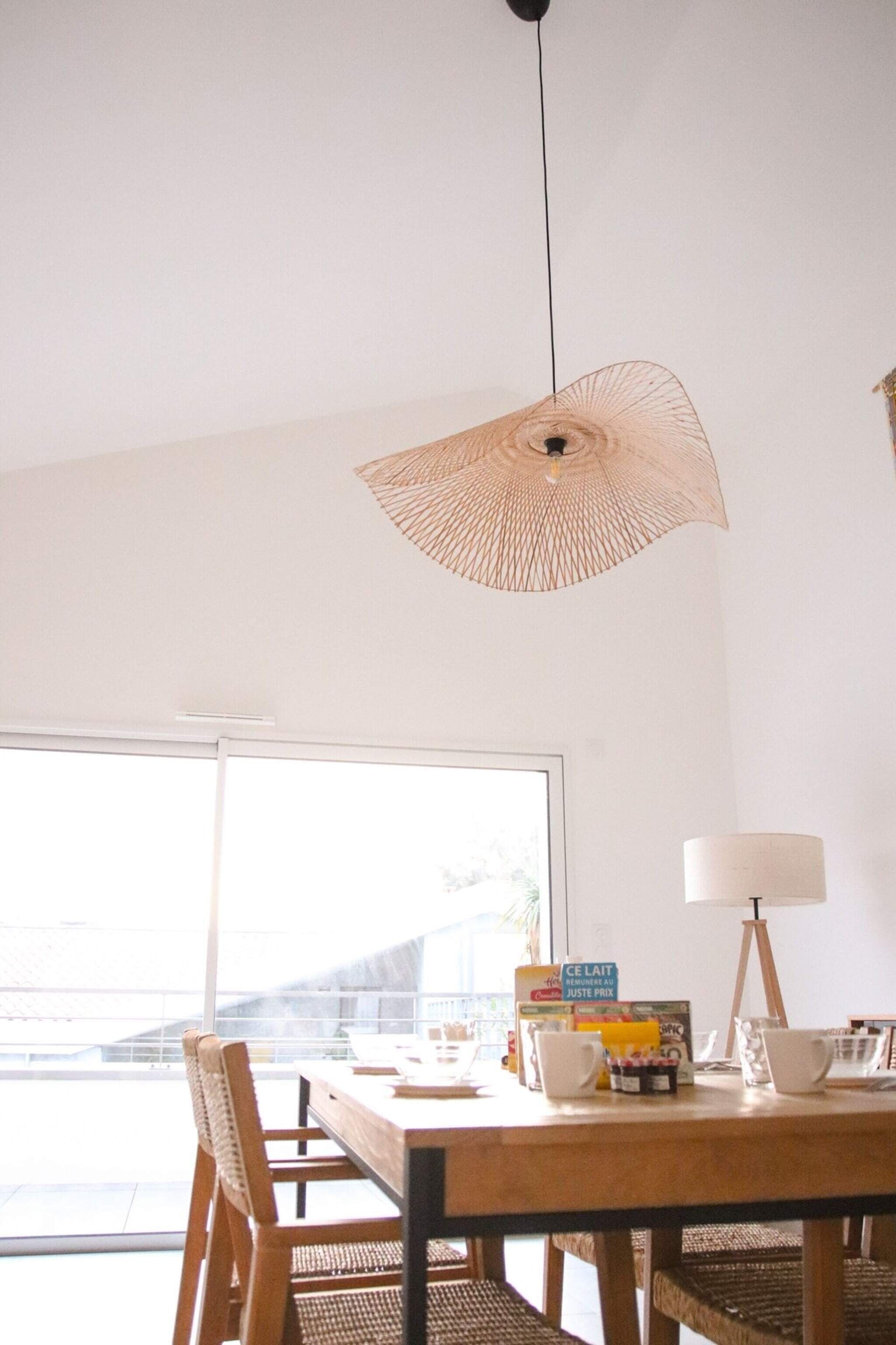 Un espace repas comprenant une table, des chaises, un luminaire suspendu et une fenêtre donnant sur les bâtiments environnants.