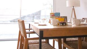 Un espace repas comprenant une table, des chaises, un luminaire suspendu et une fenêtre donnant sur les bâtiments environnants.