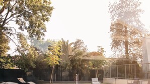 Une piscine dotée d’une terrasse en bois, entourée d’arbres et protégée par une enceinte en verre.
