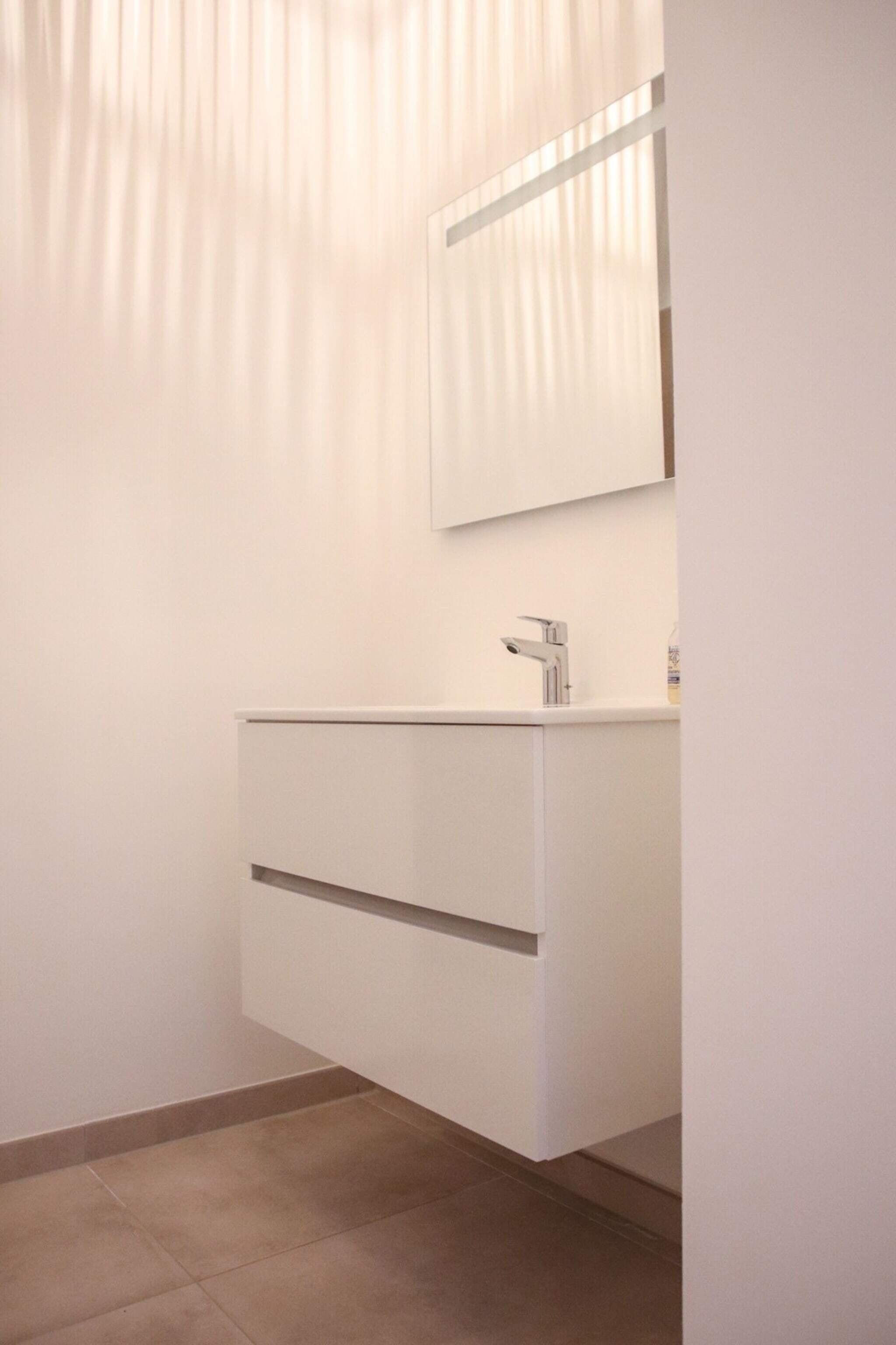 Une salle de bain moderne avec un meuble-lavabo blanc, un miroir et un robinet.