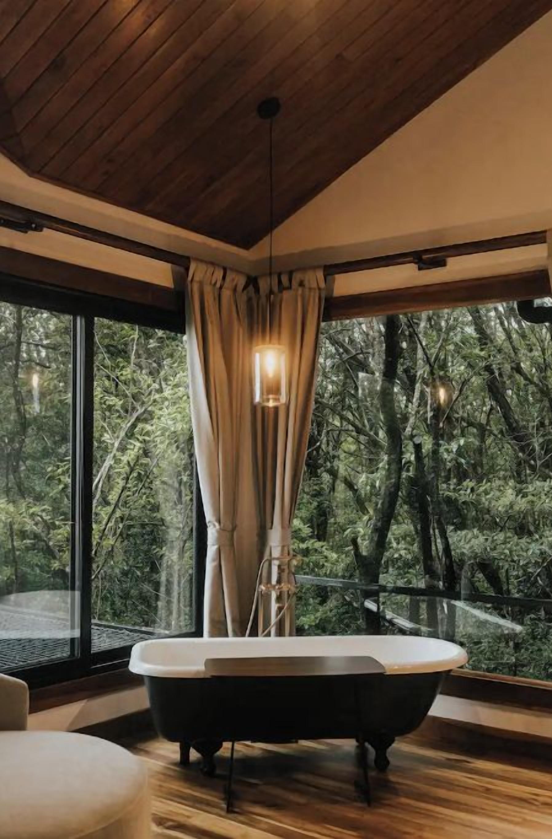Un baño moderno con una bañera independiente, ventanas amplias y vistas al bosque.