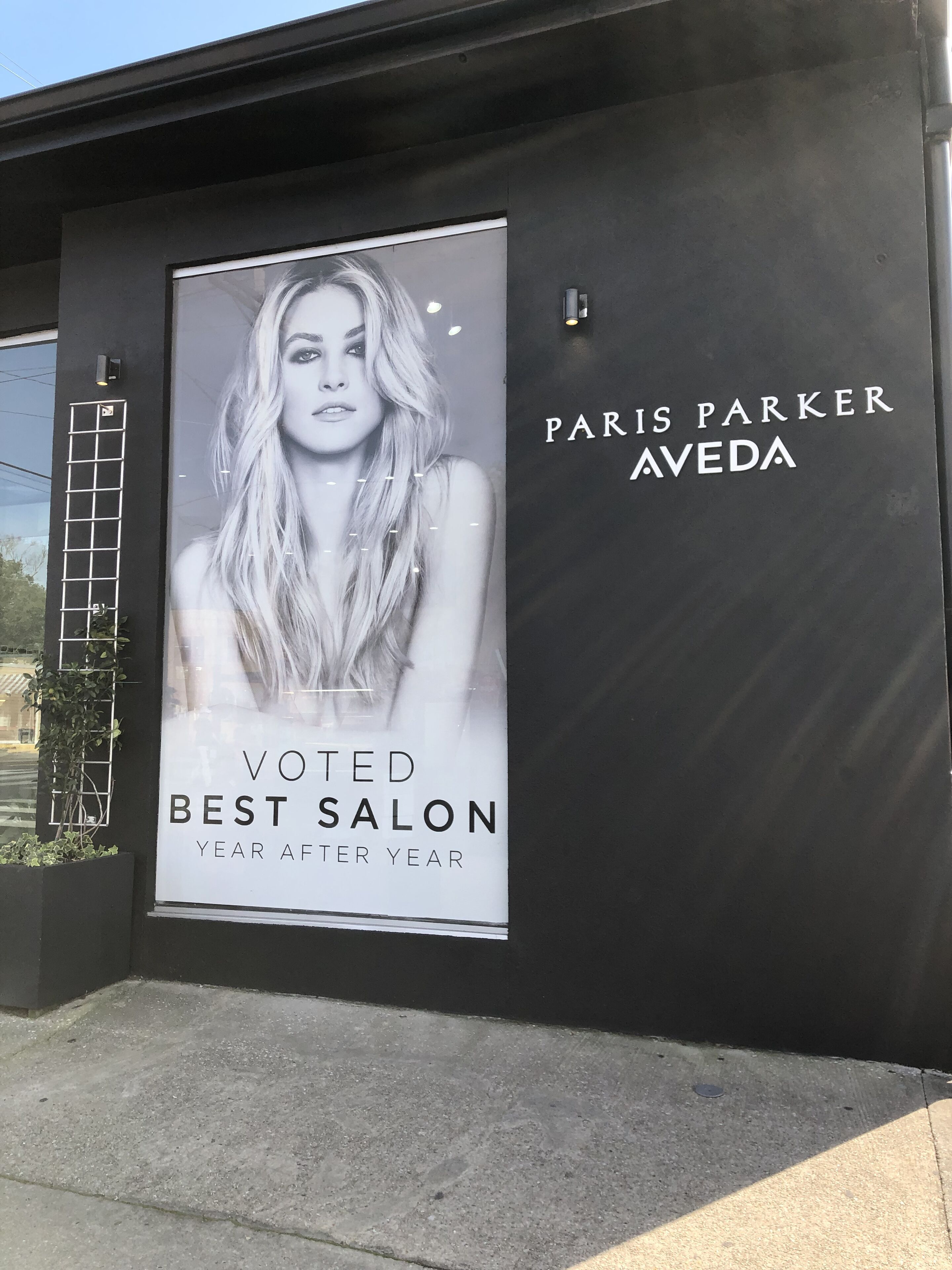 Une grande affiche publicitaire présente un salon de beauté, avec un portrait de femme en grand format et un texte indiquant qu’il a été élu meilleur salon de l’année, année après année.