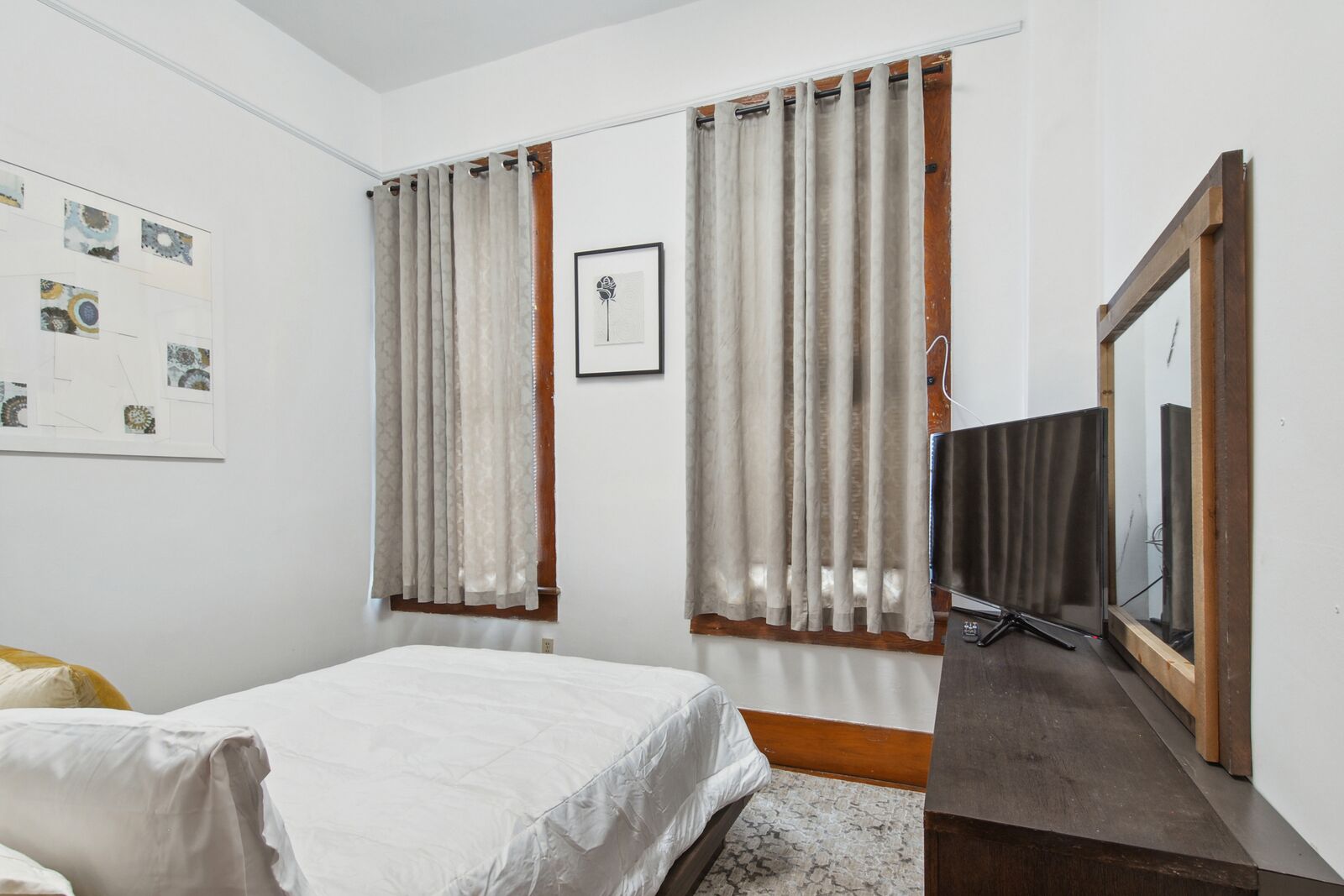 A bedroom with a bed, curtains, a framed picture, and a TV.
