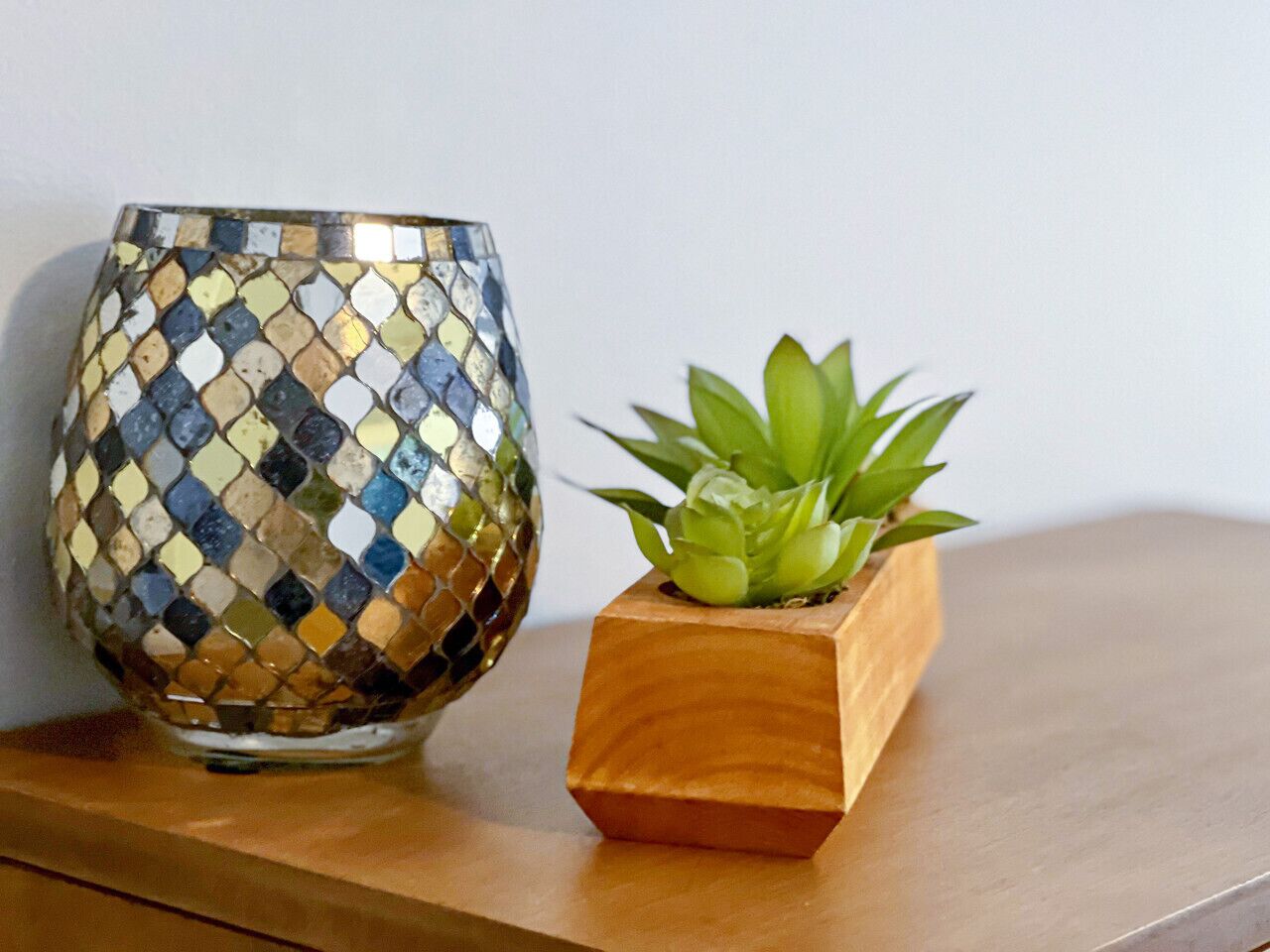 A mosaic-patterned glass bowl and a wooden planter with a succulent plant on a wooden surface.