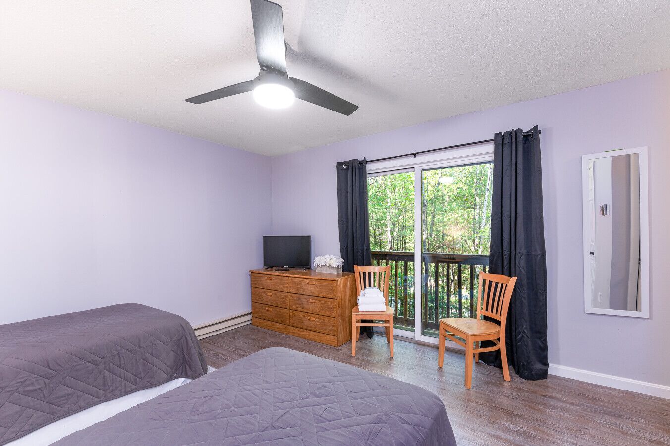 A bedroom with two beds, a TV on a wooden dresser, and a balcony with curtains.