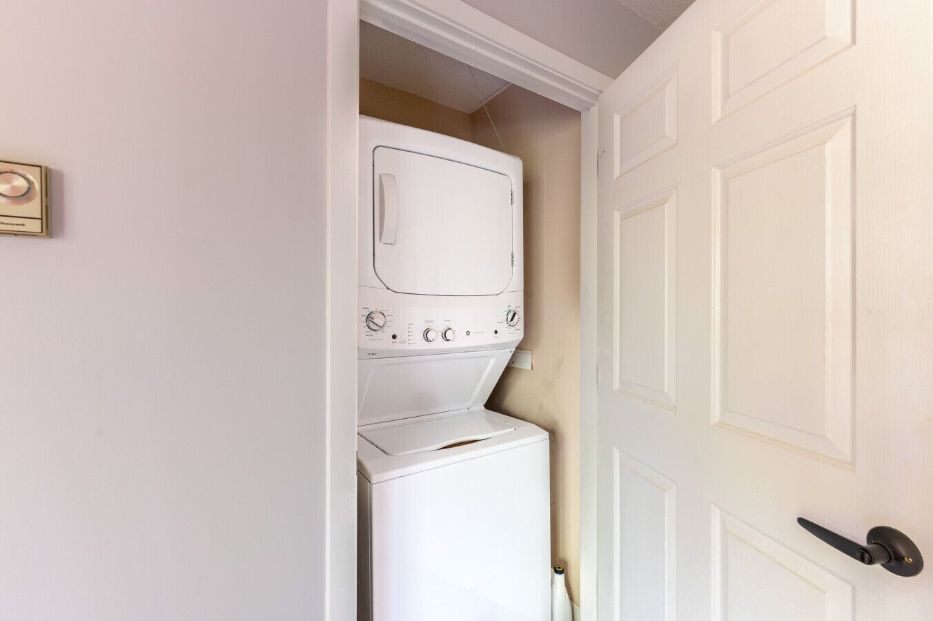 Une buanderie équipée d’un lave-linge et d’un sèche-linge, une porte avec une poignée noire et un interrupteur sur le mur.
