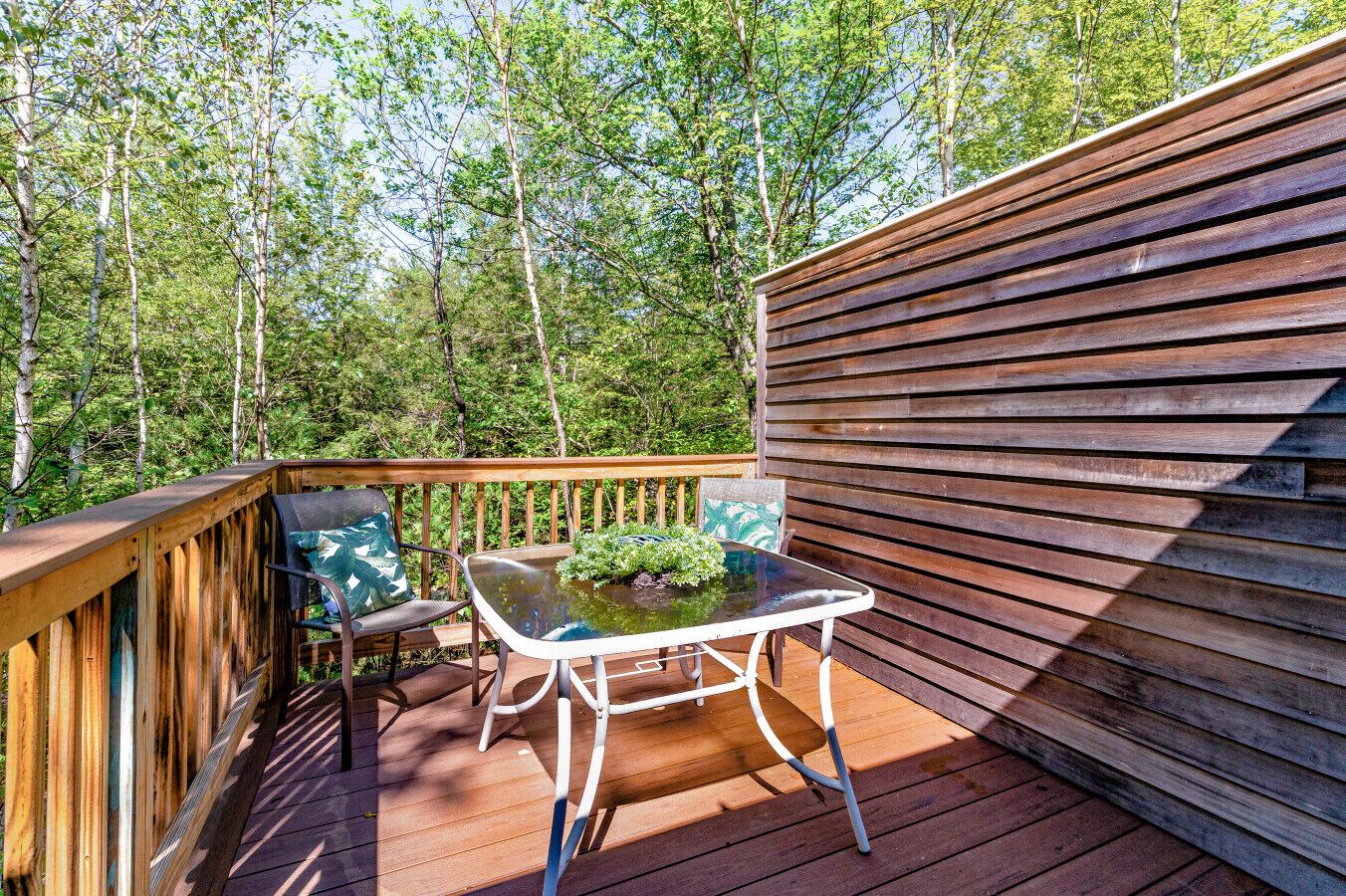 A wooden deck with a table and chairs, surrounded by a wooden fence and trees.