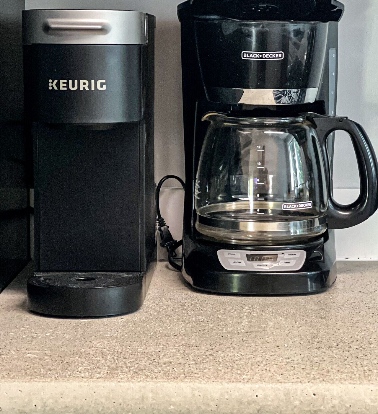 Una cafetera amb un recipient de vidre transparent i una base negra, connectada a un dispensador de càpsules de cafè negre i platejat.