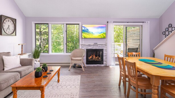 A living room with a fireplace, large windows, a TV, and a dining area.