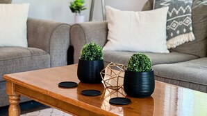 A living room with a wooden coffee table, two potted plants, and a geometric decorative piece.