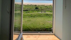 A room with a large sliding glass door leading to a balcony with a view of a beach and grassy area. - Lovely house on the beach front in Llansteffan (Carmarthen)
