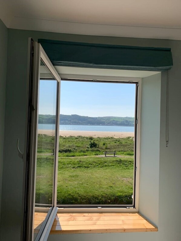 Et værelse med en stor skydedør, der fører ud til en balkon med udsigt over en strand og græsareal.