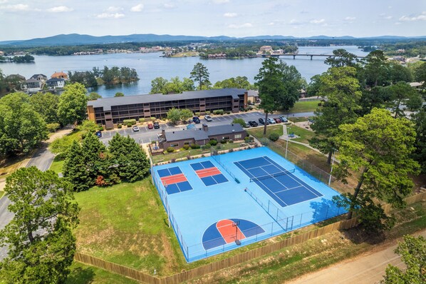 Vista aérea de un complejo deportivo con cancha de tenis, un edificio y un río al fondo.