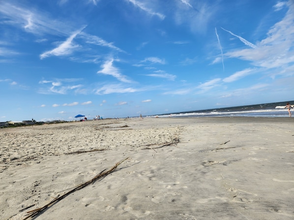 A beach with a clear sky, sandy shore, and a few people in the distance. - Historic 1940's Beach Cottage, steps to the beach! (Tybee Island)