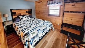 A bedroom with a wooden headboard, a quilted bedspread, a nightstand, a lamp, a window with blinds, and a wooden bench. - Cozy Adirondack Retreat sleeps 5, 3 miles to Gore skiing, hiking, rafting (North Creek)