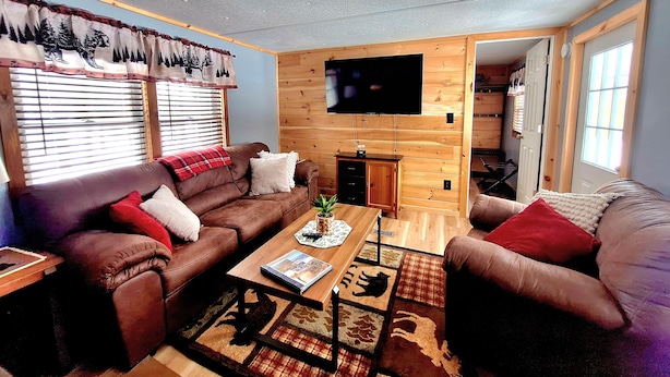 A cozy living room with a brown leather sofa, a wooden coffee table, and a TV mounted on the wall. - Cozy Adirondack Retreat sleeps 5, 3 miles to Gore skiing, hiking, rafting (North Creek)
