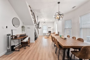 Una cocina moderna con una isla central, un comedor con una larga mesa de madera, y una escalera que sube a un nivel superior.