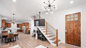 A spacious living area with a wooden staircase, a dining table, and a kitchen in the background.