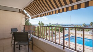 A balcony with a view of a swimming pool and a cruise ship in the distance.